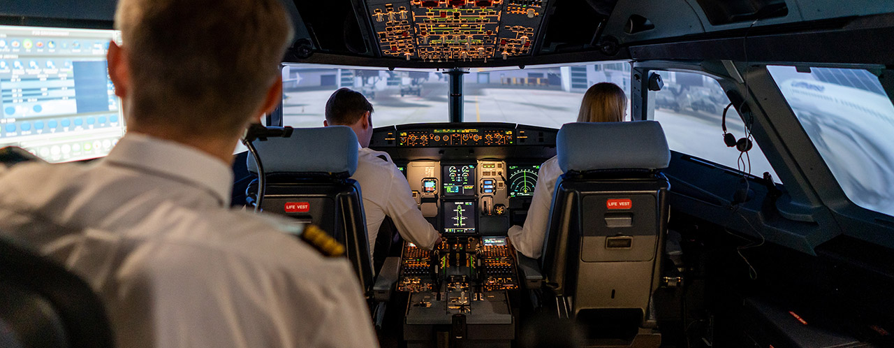 View into a cockpit simulator with two pilots and an instructor